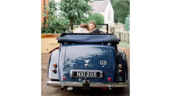 Rear view of the vehicle with Bride and Groom inside the vehicle with the roof down kissing
